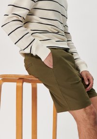Khaki šortky vyrobené z bavlny, s bočními kapsami a uvolněným střihem. V páru s proužkovanou krémovou a námořnickou dlouhým rukávem.