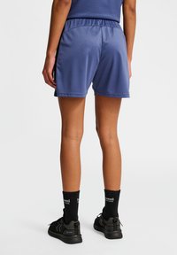 Blauwe sportieve shorts met een elastische tailleband, een gladde textuur en accenten op de zijpanelen. Gekleed met zwarte schoenen en sokken.