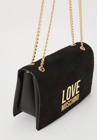 Musta käsilaukku, jossa on tilkkutekstuuri, kultaketjuolkaimet ja edessä kultakirjaimin "LOVE MOSCHINO" -logo.
