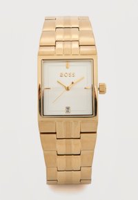 Ρολόι χειρός ορθογώνιου σχήματος με χρυσό τόνο, λευκό καντράν, χρυσά δείκτες, παράθυρο ημερομηνίας στις 6 η ώρα και ενωμένο μεταλλικό λουρί.