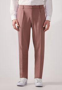 Rosenfarbene Hose aus leichtem Stoff mit tailliertem Schnitt, Falten vorne und elastischem Bund, kombiniert mit weißen Sneakers.