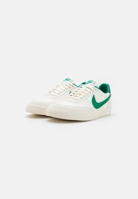 Valged sneakers roheliste detailidega, millel on sile nahk, lamedad paelad, pehmendusega kaelus ja tekstureeritud kummiseid.