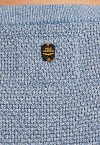 Pull en tricot bleu clair avec un motif texturé et une étiquette noire et dorée portant l'inscription "PME LEGEND".