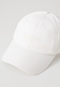 Hvid baseballcap i stof med et broderet "tommy jeans" logo i matchende hvid. Bøjet skygge og syede detaljer.