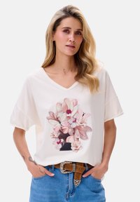 Witte V-hals t-shirt met een bloemig ontwerp in roze en crèmekleuren, met een relaxte pasvorm en korte mouwen, gecombineerd met blauwe denim.