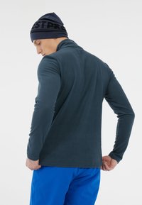 Mørkeblå fleecepullover med høj krave og lange ærmer. Stoffet er blødt med en let struktureret overflade. Sammen med lyseblå bukser.