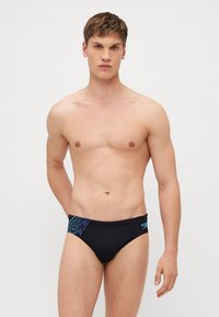 Sorte svømmebukser med blå og turkise skrå striper på den ene siden. Laget av glatt, elastisk materiale. Enkel, figursydd design.