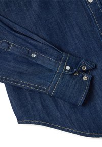 Denim shirt cuff with yellow stitching and closed silver snap buttons on a white background.