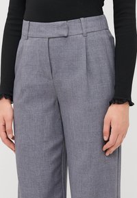Lichtgrijze op maat gemaakte broek met voorplooien, een gladde textuur en een tailleband. Gecombineerd met een zwart geribbeld langemouwen top met gerimpelde manchetten.