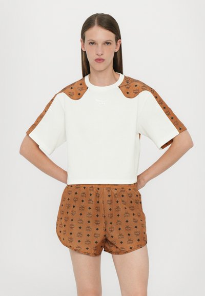 Gecropptes weißes Sweatshirt mit braunem Muster an den Ärmeln und Shorts mit MCM-Logo und Diamantmustern. Weicher Stoff, lockere Passform.
