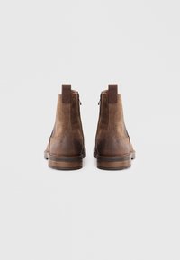 Botas de tobillo de cuero marrón con un acabado liso y ante, que presentan una cremallera en la parte trasera y un detalle de tacón marrón en contraste.