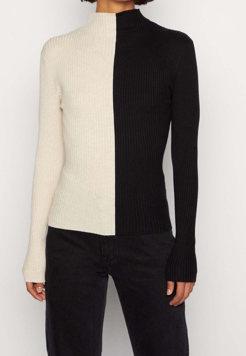 Geripptes Rollkragenpullover mit einem geteilten Design in Creme und Schwarz, langen Ärmeln und einer schlanken Passform. Akzentuiert durch kontrastierende Farben.