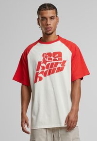 Red and white oversized t-shirt with a graphic print. Short raglan sleeves, soft fabric, and a relaxed fit. Bold logo in red on the front.