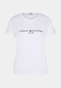Biała koszulka z krótkim rękawem z logo "Tommy Hilfiger EST. 1985" oraz emblematem flagi w kolorach czerwonym, białym i niebieskim na wysokości klatki piersiowej.