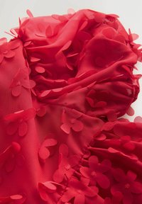 Roter transparenter Stoff mit geschichteten, aufgenähten Blumenelementen. Die Blumen sind in der Mitte mit kleinen runden Perlen akzentuiert, was zusätzliche Textur schafft.
