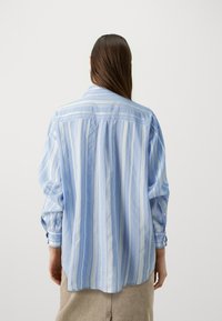 Camicia a righe blu e bianche, tessuto leggero, vestibilità rilassata, polsini con bottoni, cucitura del passante sul retro e orlo curvo.