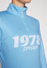 Pullover azzurro chiaro a mezza zip con un motivo lavorato a maglia. Presenta un alto colletto e una grande grafica "1978" in bianco, marchiata "Spyder."