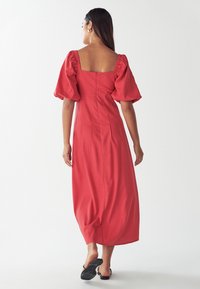 Rdeča maksi obleka s puhastimi rokavi in kvadratnim izrezom. Gladek material, prilega se v pasu, ter padajoča krila do gležnjev.