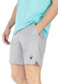 Pantalones cortos deportivos grises con una tela ligera, bolsillos laterales y un logo de araña negro en la pierna izquierda. Acompañados de una camiseta de color azul claro.
