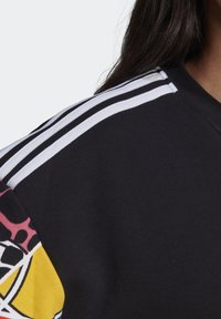 Sweatshirt noir avec des rayures blanches sur l'épaule, arborant un motif graphique coloré en rose, jaune et noir sur une manche.