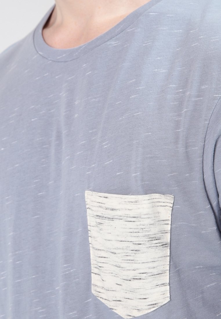 Ljust grå crew-neck t-shirt i mjukt material, med en texturerad vit ficka med ett subtilt mönster.