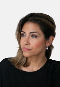 Svart langermet topp, løs passform. Modellen har middels langt brunt hår, bærer en enkel perleøredobb, nøytral sminke og et konsentrert uttrykk.