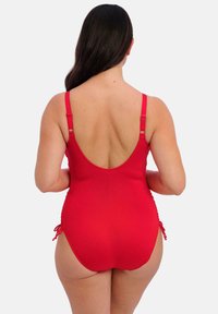 Maillot de bain une pièce rouge avec des bretelles réglables, un dos plongeant et des liens sur les côtés. Tissu lisse de couleur unie avec un minimum de détails.