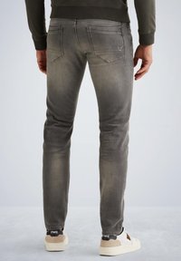 Sivé slim-fit džínsy s mierne vyblednutou textúrou, so zadnými vreckami a detailom loga. Nosené s bielymi a béžovými teniskami.
