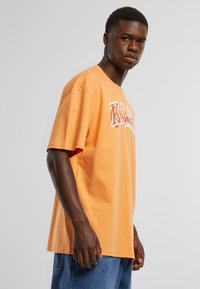 Orange bomulds T-shirt med en afslappet pasform, der har fed hvide tekstgrafikker. Korte ærmer og rund halsudskæring med en blød struktur.