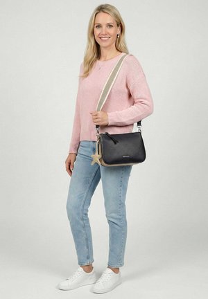 Nainen, jolla on päällään vaaleanpunainen neulepaita ja vaaleansiniset farkut, pitää käsissään mustaa olkalaukkua, jossa on leveä raidallinen hihna ja tähtimuotoinen avaimenperä.