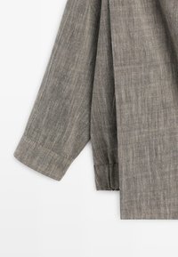 Manica di giacca in tessuto grigio strutturato con dettagli di cucitura visibili e polsino, esposta su uno sfondo bianco.