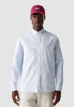 Hellblaues Button-Up-Hemd mit bestickten Mustern, langen Ärmeln und spitzem Kragen, getragen mit einer kastanienbraunen Baseballmütze.