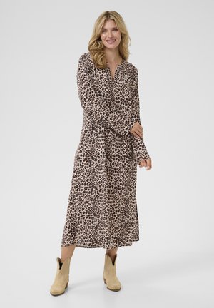 Robe imprimé léopard en beige clair et marron foncé, avec des manches longues et une longueur mi-mollet. Portée avec des bottines à la cheville beige clair.