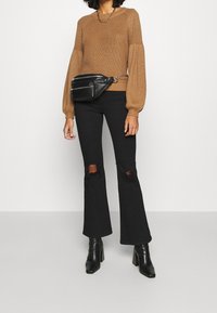 Brun stickad tröja med ballongsärmar, kombinerad med svarta utsvängda jeans med knäslitsar, och svarta klackade ankle boots.