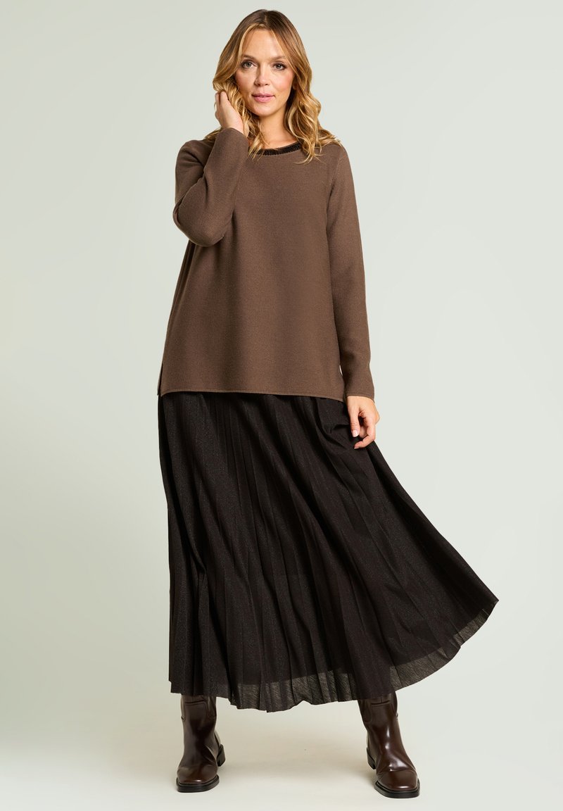 Pull marron à coupe décontractée, jupe longue noire plissée, et bottes montantes marron foncé. Texture lisse, design en couches, et éclat subtil.