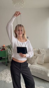 Black leather crossbody purse with a silver chain strap; rectangular shape with a smooth texture and minimalistic design.