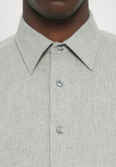 Lys grå skjorte med knapper i teksturert stoff, med klassisk krage og to-knapps plissering. Enkel design, ingen mønstre.