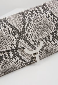 Kabelka v černobílé hadí potisku s texturovaným povrchem, s kovovým uzávěrem v stříbrné barvě a ostrým designem.