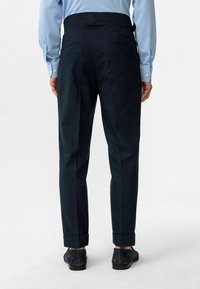 Donkerblauwe broek met een getailleerde pasvorm, met een hoge tailleband, twee achterzakken en opgerolde mouwen, gecombineerd met donkere schoenen.