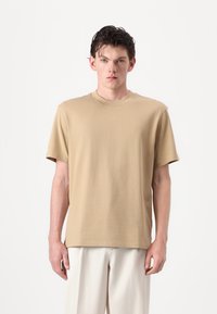 Beige Baumwoll-T-Shirt mit Rundhalsausschnitt, kurzen Ärmeln und dezentem "HUGO"-Logo auf der Brust, in entspannter Passform und angenehmer Textur.