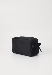 Svart rektangulær toalettrenset bag laget av slitesterkt stoff, med glidelås og en sidesløyfe for enkel bæring.