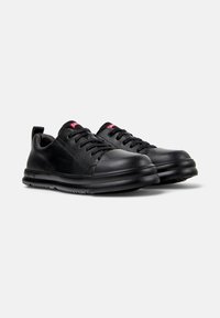 Svarta sneakers med en slät yta och förstärkt tå, med snörning och en diskret logotyp på tungan.