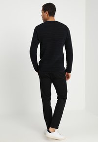 Pulover tricotat cu dungi negre, cu mâneci lungi și decolteu rotund, asortat cu pantaloni negri și adidași albi. Detaliu de țesătură texturată vizibil.