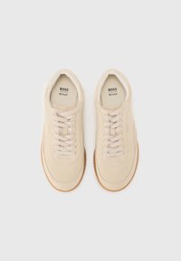Beige sneakers med skinnoverdel, rund tå, flate lisser og kontrasterende gummisåle. Logo vist på tungen.
