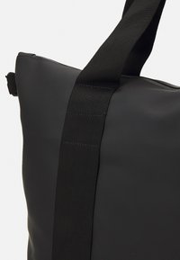 Borsa a tracolla nera con finitura liscia e opaca e una tracolla nera texturizzata. Caratterizzata da una forma rettangolare e un design minimalista.