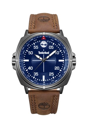 Analógové hodinky Timberland s modrým ciferníkom, bielymi značkami, strieborným puzdrom a hnedým koženým remienkom s vyrazeným logom stromu.