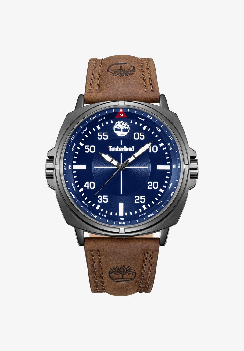 Montre analogique Timberland avec cadran bleu, index blancs, boîtier argenté et bracelet en cuir marron embossé du logo arbre.