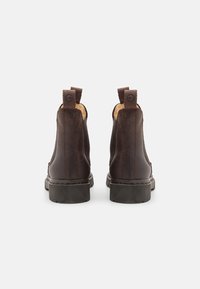 Botas de piel marrón hasta el tobillo con un acabado suave, lengüetas en la parte trasera y una suela de goma texturizada, que muestran un diseño clásico.