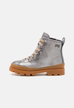 Bottine argentée métallique avec lacets beiges, en cuir texturé, semelle en caoutchouc et un accent noir à l'arrière. Présente un motif de semelle prononcé.