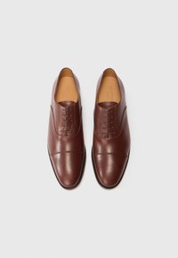 Un par de zapatos de vestir Oxford de cuero marrón con cordones cerrados y puntera, exhibidos uno al lado del otro sobre un fondo blanco.